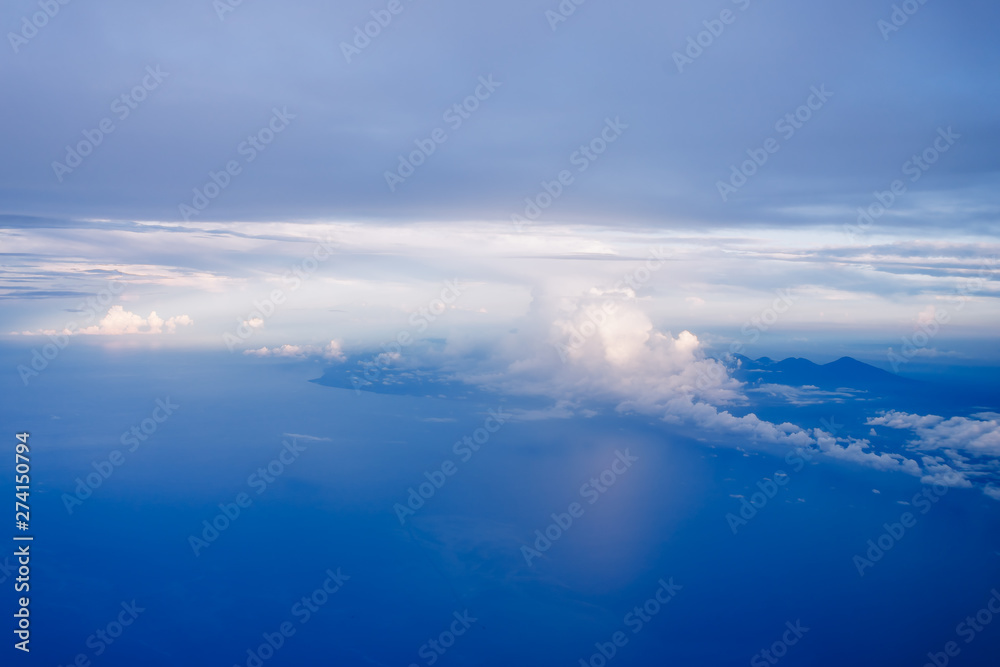 Plane window view with blue sky and clouds. Clouds and sky as seen through window of an aircraft. View of beautiful cloud, ocean and city from the airplane.