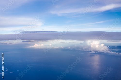 Plane window view with blue sky and clouds. Clouds and sky as seen through window of an aircraft. View of beautiful cloud, ocean and city from the airplane. © Anastasia