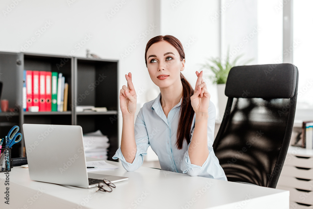 Woman working in the office, praying and holding fingers crossed that she will achieve success in business