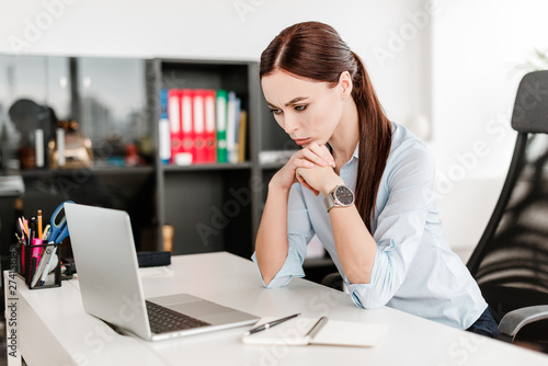 Woman looking in the laptop in the office where she works and thinks and makes business decisions