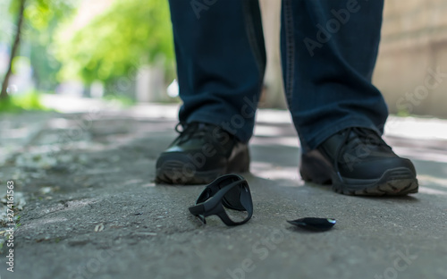 View of the feet of a man who stands on an asphalt road on the background of fallen and broken sunglasses