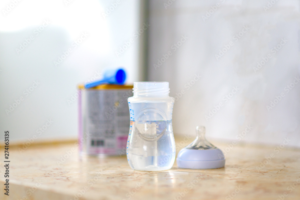 Preparation of mixture baby feeding on marble background in morning kitchen. Feeding bottle with water and baby milk formula with spoon on table.Selective focus. Preparation of mixture baby feeding on marble background in morning kitchen. Feeding bottle with water and baby milk formula with spoon on table.Selective focus.