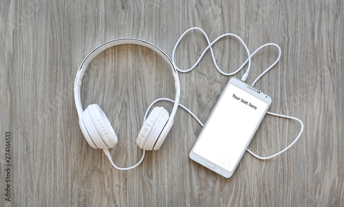 Headphones and smartphone with word "Your text here" on white screen against wooden background