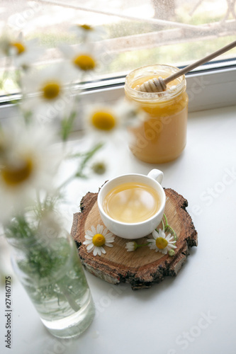 Cup of herbal tea, honey and chamomile on the white windowsiil, summer tea time, remedy aternative photo