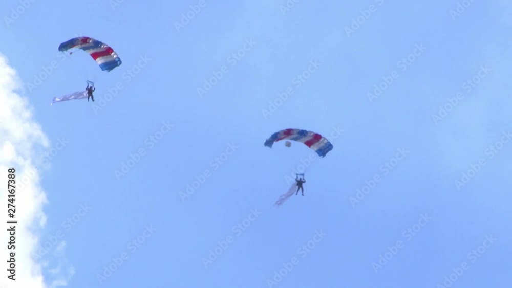 Two people flying with parachutes at an air show in Berlin. The weather is sunny with a few clouds. Two people flying with parachutes at an air show in Berlin. The weather is sunny with a few clouds.