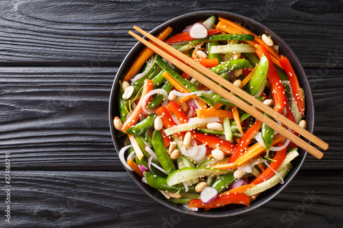 Salad of cucumbers, peppers, carrots, pea pods with sesame and peanuts close-up on a plate. horizontal top view