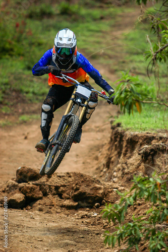 A professional down hill cyclist racer jumping and doing a swipe on his full suspension carbon bike