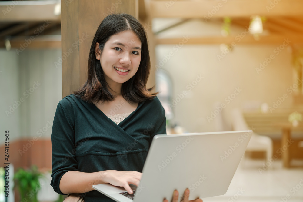 Closeup Asian beautiful woman Put on a black shirt and stand against the wooden pillar in the middle of the house. Use a laptop computer to work happily Closeup Asian beautiful woman Put on a black shirt and stand against the wooden pillar in the middle of the house. Use a laptop computer to work happily