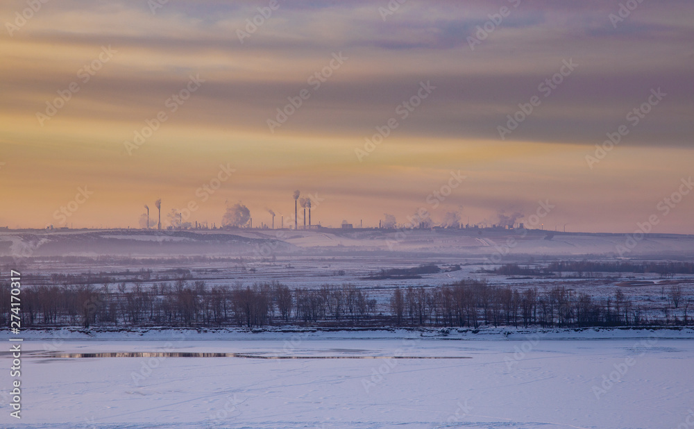 Fototapeta premium Panoramic view on frozen river and forest on hill in winter during sunset from hill