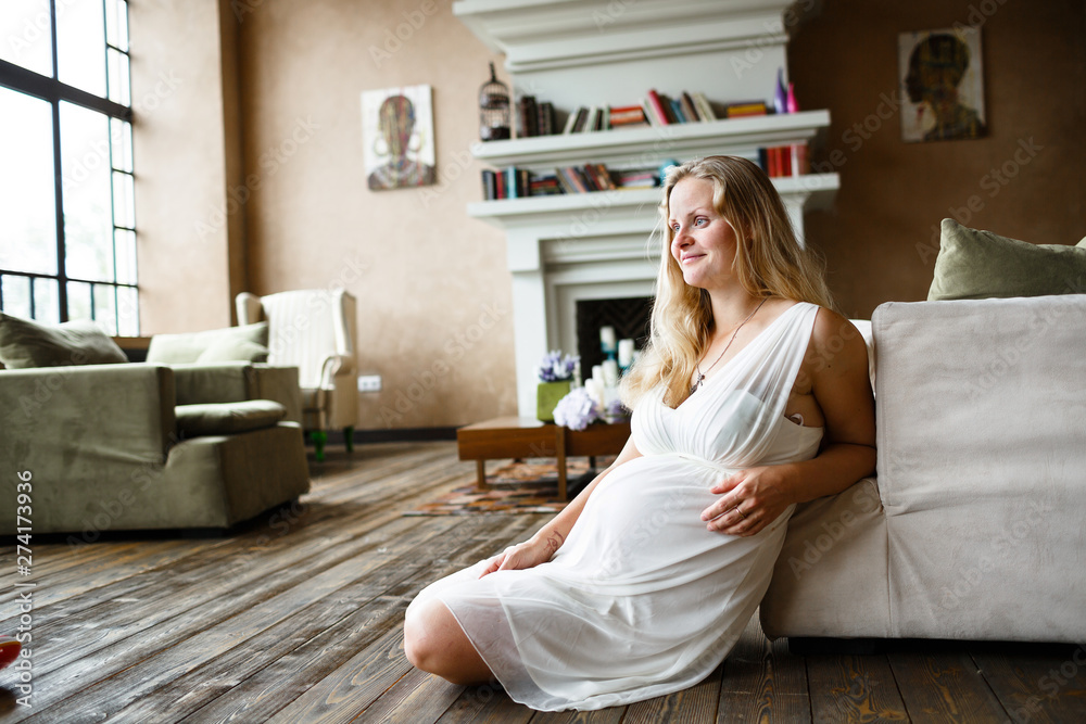 Portrait of a beautiful long-haired pregnant blonde, gracefully sitting on floor Portrait of a beautiful long-haired pregnant blonde, gracefully sitting on floor