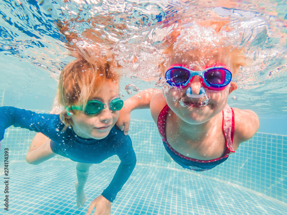 Kids having fun playing underwater in swimming pool on summer vacation