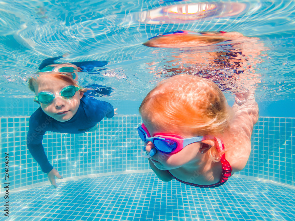 Kids having fun playing underwater in swimming pool on summer vacation