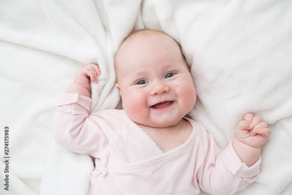 Newborn baby girl posed on her back, on blanket of fur, smiling looking at camera Newborn baby girl posed on her back, on blanket of fur, smiling looking at camera