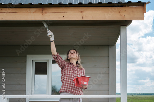 young European woman painting the veranda of a new wooden house