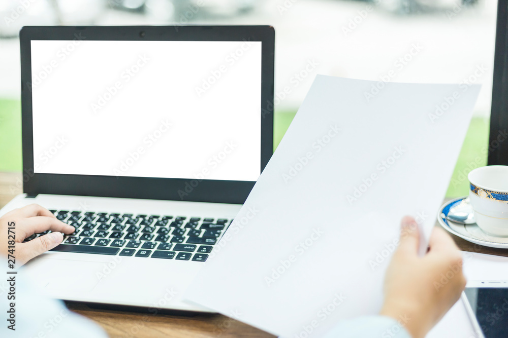 Close-up of business female working with laptop and Hand holding of blank white document in coffee shop like the background. Close-up of business female working with laptop and Hand holding of blank white document in coffee shop like the background.
