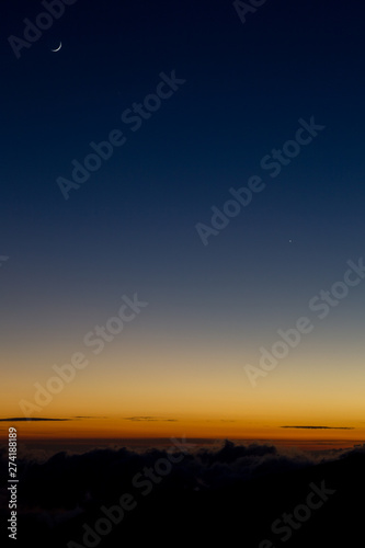 Crescent moon over the bright orange horizon lit by the last light of sunset at the Mauna Kea on Big Island  Hawaii  USA.