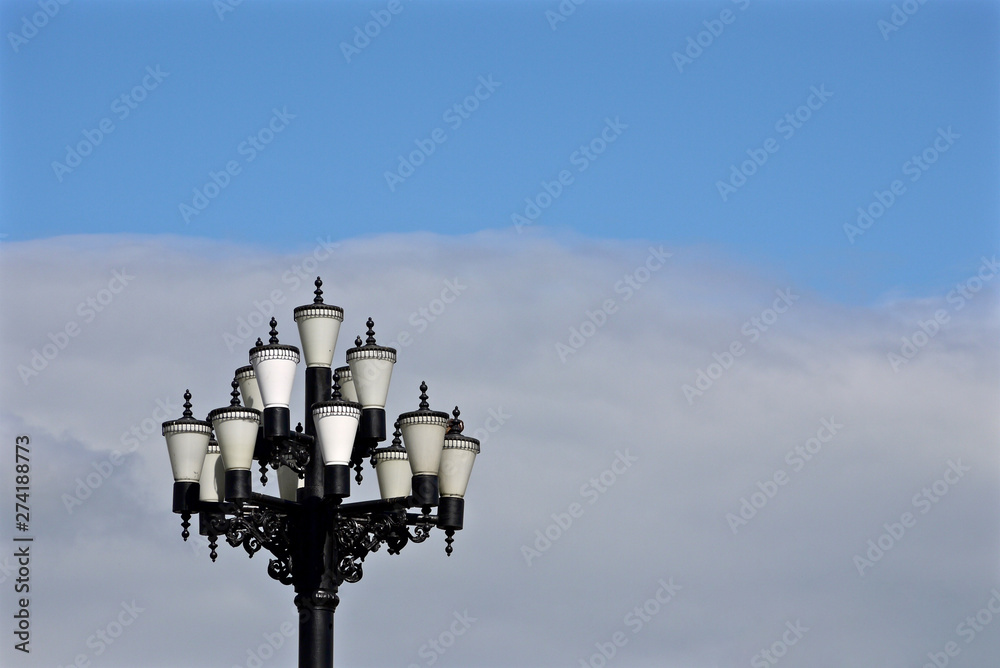 pretty street lamp with many white glass covers on background of blue cloudy sky