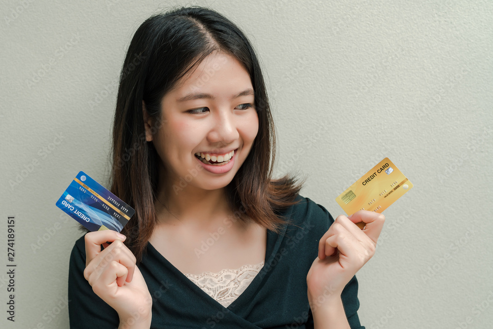 Asian beautiful woman Wearing a black shirt There are credit cards in both hands. Happy face Standing in the gray wall Asian beautiful woman Wearing a black shirt There are credit cards in both hands. Happy face Standing in the gray wall