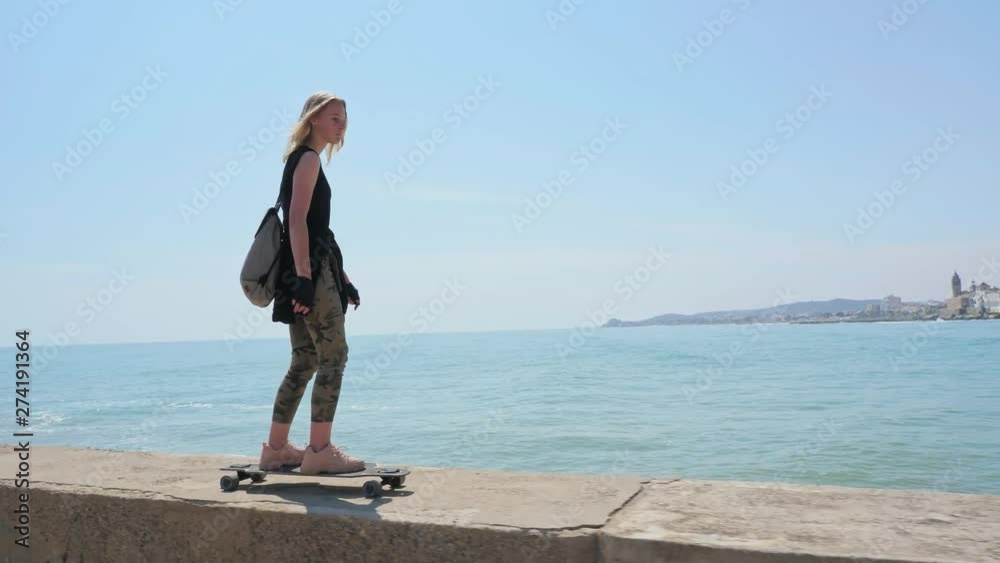 A beautiful blonde girl on skateboard in summer hot day on seafront A beautiful blonde girl on skateboard in summer hot day on seafront