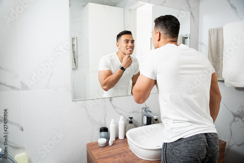 Smiling young man touching his chin before mirror