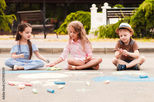 Small children draw in chalk among the city street.