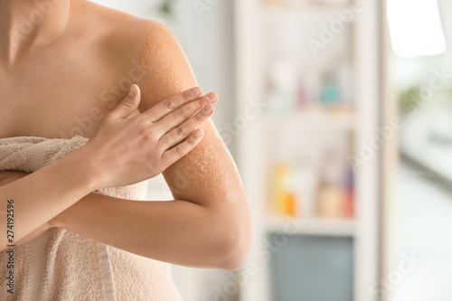 Beautiful young woman applying body scrub at home