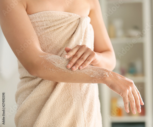 Beautiful young woman applying body scrub at home