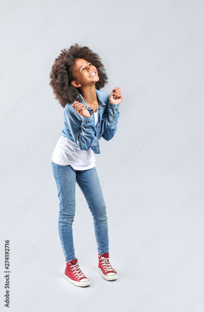 Stylish African-American girl in jeans clothes on grey background