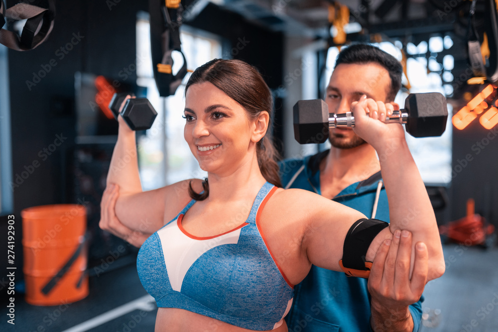 Fototapeta premium Trainer helping positive woman doing exercises for arms