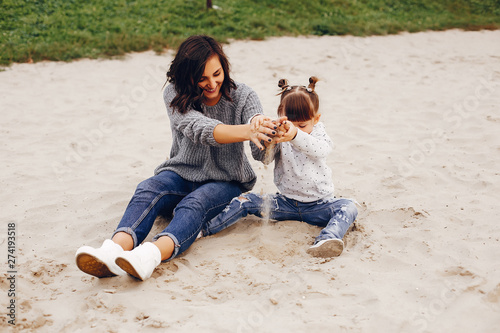 Family sitting on the sand. Mother in a gray sweater. Cute little girl