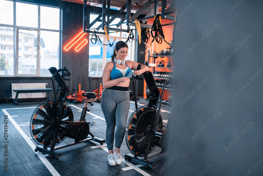 Overweight woman wearing top using her phone in gym