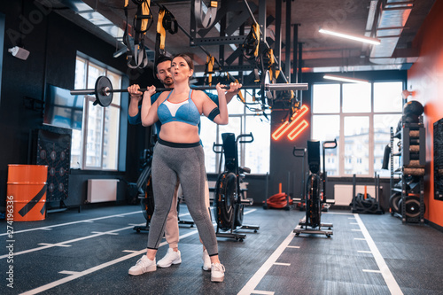 Woman hardly breathing after lifting barbell standing near trainer