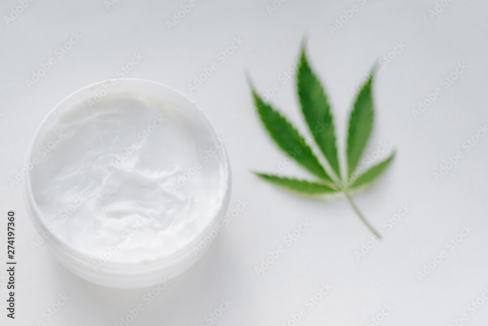 Open jar of hemp cream with cannabis leaf on white isolated background. Top view with moisturizing lotion from natural products containing CBD. Flat composition with marijuana and copy space Open jar of hemp cream with cannabis leaf on white isolated background. Top view with moisturizing lotion from natural products containing CBD. Flat composition with marijuana and copy space