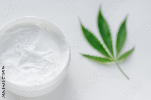 Top view jar of hemp cream with cannabis green leaf on white background. Moisturizing lotion from natural products containing CBD