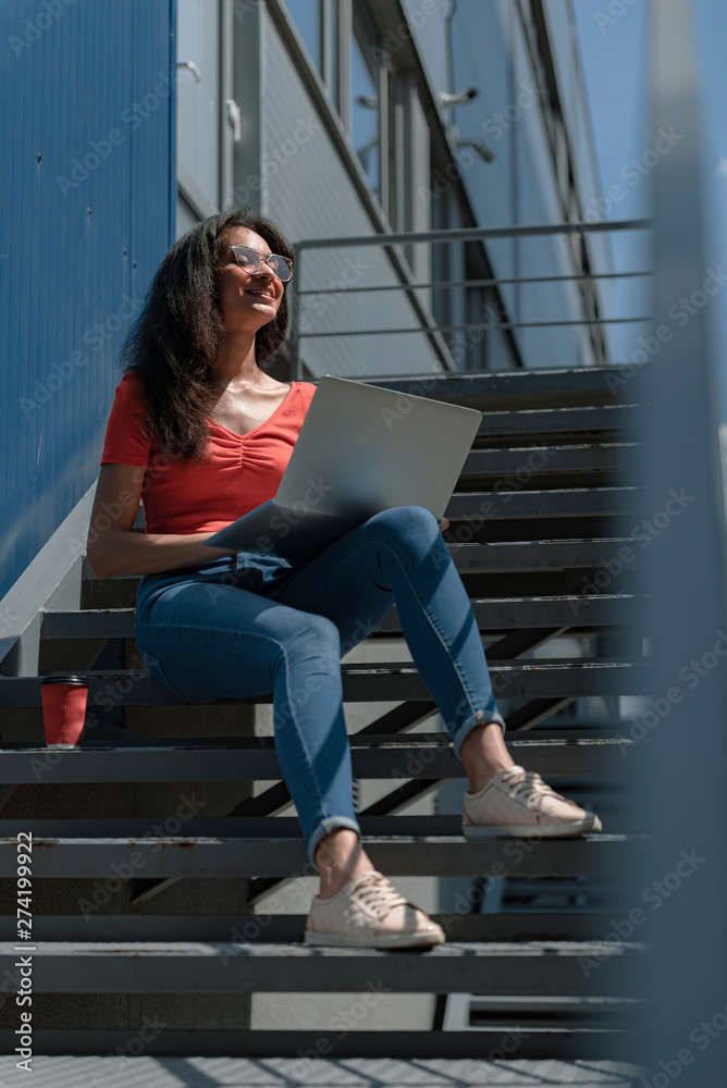 Charming young woman with notebook on her laps sitting on stairs
