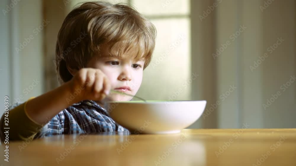 The child in the kitchen at the table eating. Little boy having breakfast in the kitchen. Happy baby boy spoon eats itself. Baby eating food on kitchen. The child in the kitchen at the table eating. Little boy having breakfast in the kitchen. Happy baby boy spoon eats itself. Baby eating food on kitchen.