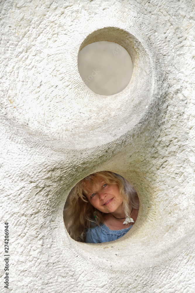 Reife, blonde Frau schaut durch Loch in Sandstein Fassade foto de Stock Adobe Stock