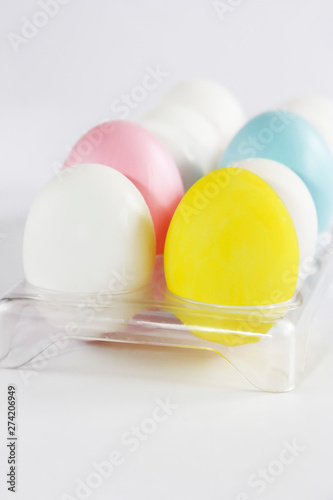 multi-colored white yellow pink blue chicken eggs in a container