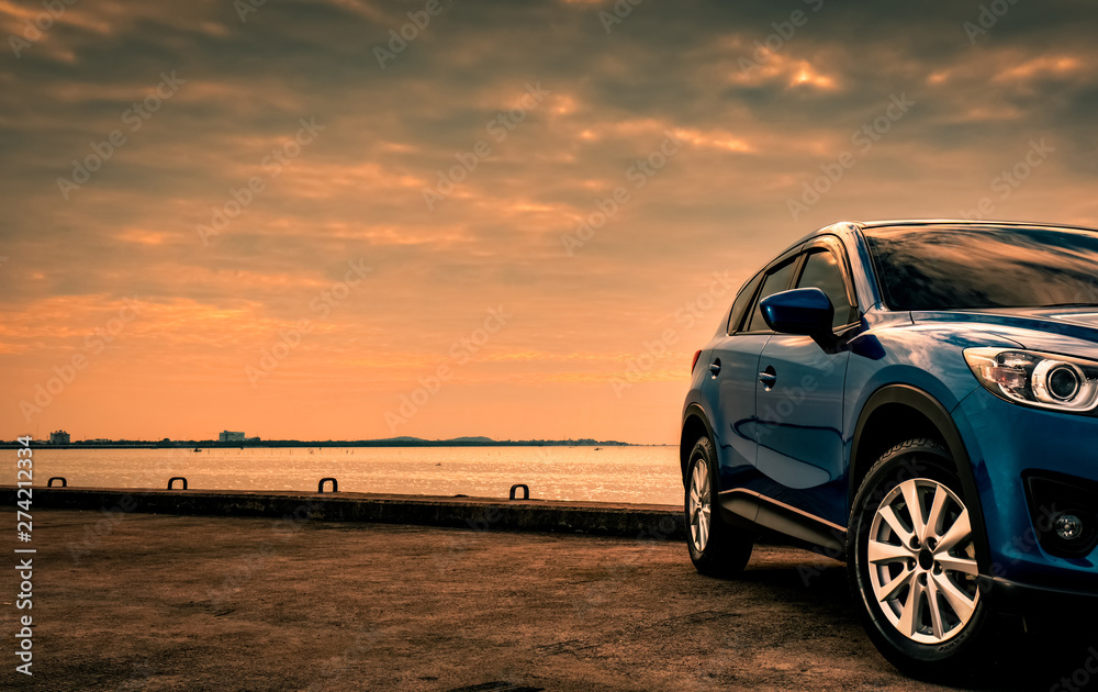Blue compact SUV car with sport and modern design parked on concrete road by the sea at sunset in the evening. Hybrid and electric car technology concept. Car parking space. Automotive industry. - obrazy, fototapety, plakaty 