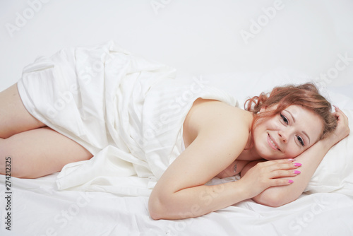 beautiful young girl is lying on a white bed and enjoying the morning. charming caucasian woman is happy and relaxing. sleepy and lazy person slowly posing alone.