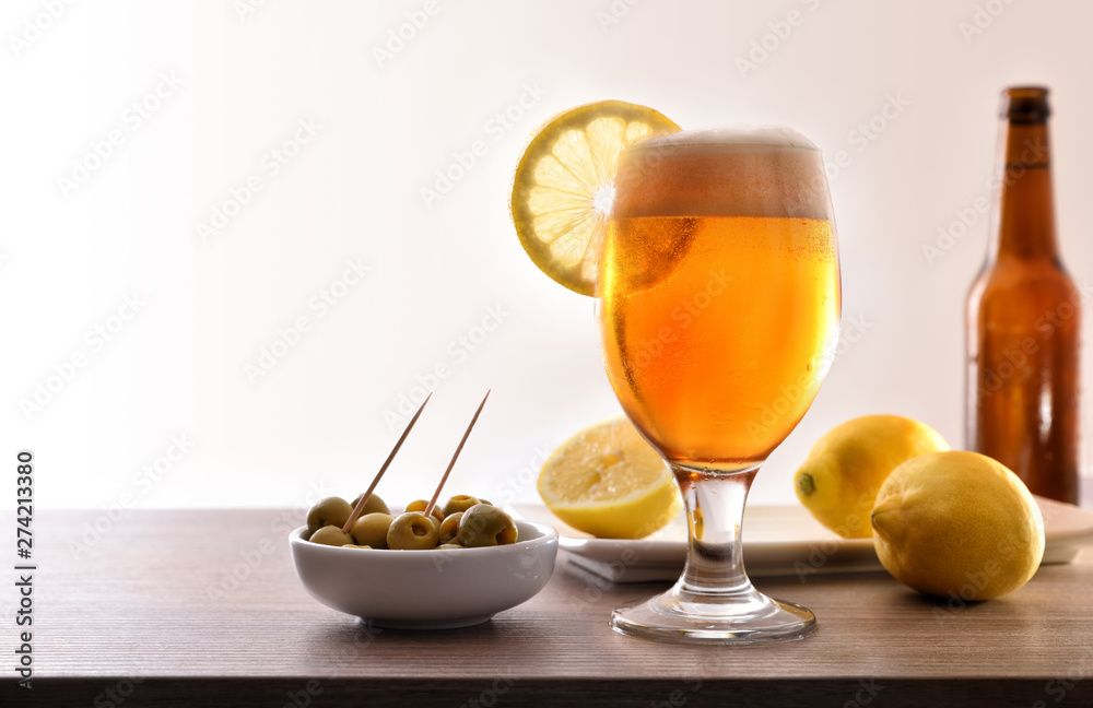 Glass of beer with lemon and appetizer on table white Glass of beer with lemon and appetizer on table white