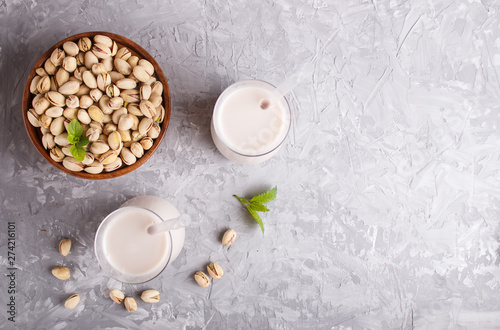 Organic non dairy pistachio milk in glass and wooden plate with pistachionuts on a gray concrete background. photo