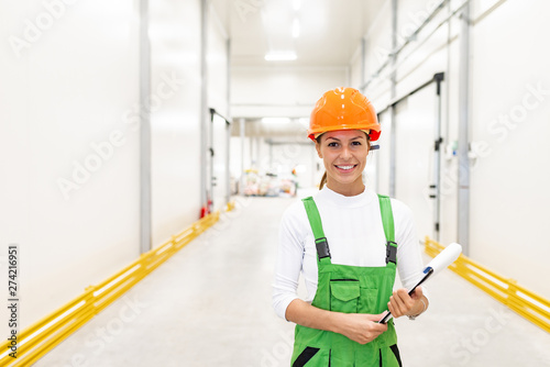 Portrait of a young female worker in protective work wear, holding clipboard and smiling at camera.