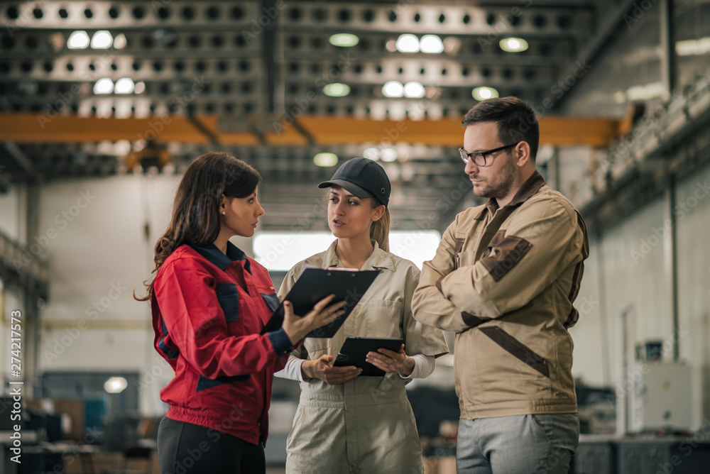 Three industrial workers discussing business at factory hall.