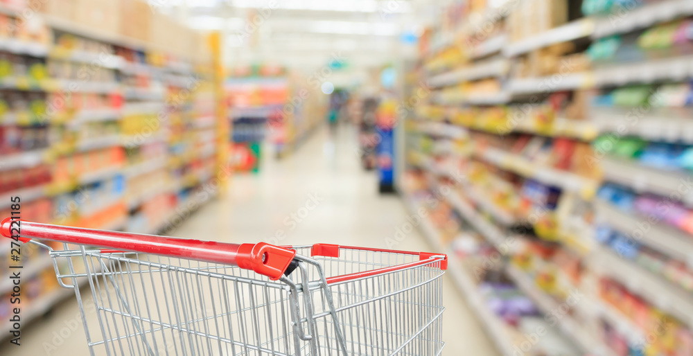 Supermarket aisle blurred background with empty red shopping cart