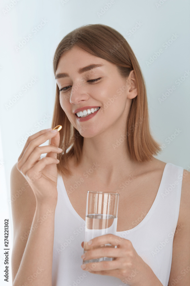 Woman taking vitamin pill with glass of fresh water indoors Woman taking vitamin pill with glass of fresh water indoors