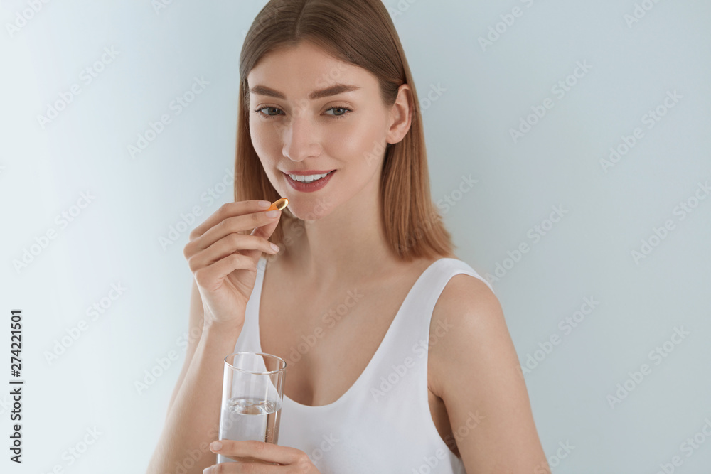 Woman taking vitamin pill with glass of fresh water indoors Woman taking vitamin pill with glass of fresh water indoors