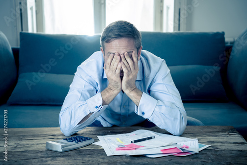 Upset man in stress paying bills counting finance with calculator bank papers expenses and payments photo