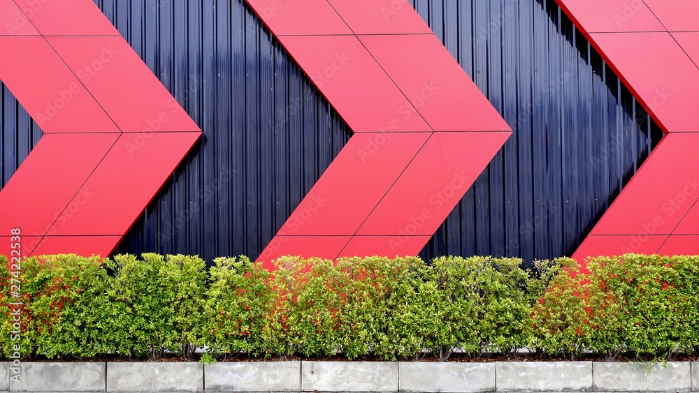 Part of red arrows pattern on black corrugated metal sheet wall background  behing green bush wall in exterior architecture decoration design concept  Stock Photo | Adobe Stock