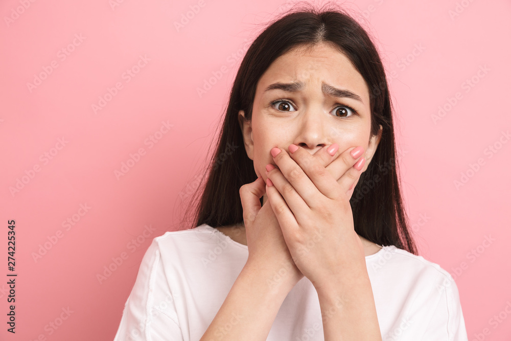 Portrait closeup of scared unhappy girl with long dark hair looking at camera and covering her mouth Portrait closeup of scared unhappy girl with long dark hair looking at camera and covering her mouth